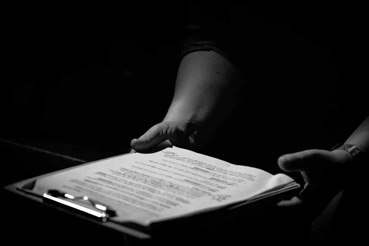 Mâini așază un set de documente pe un clipboard, într-o încăpere întunecată