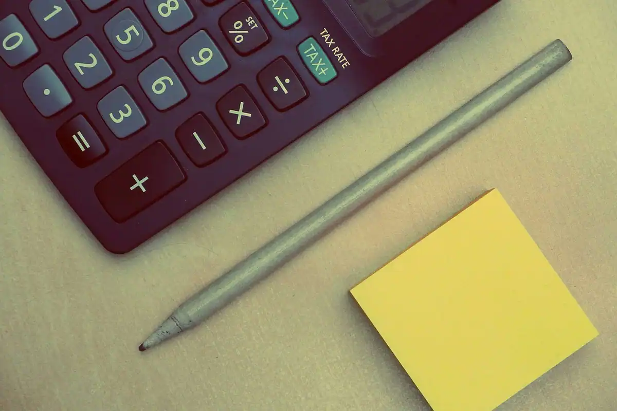 Calculator roșu, creion și o notiță galbenă, așezate pe un birou