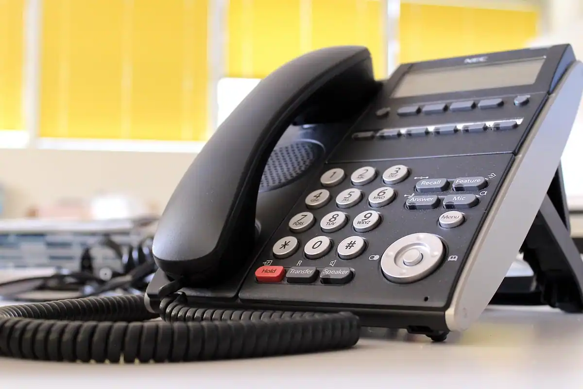 Telefon fix de birou, negru, cu fir spiralat, pe un blat alb