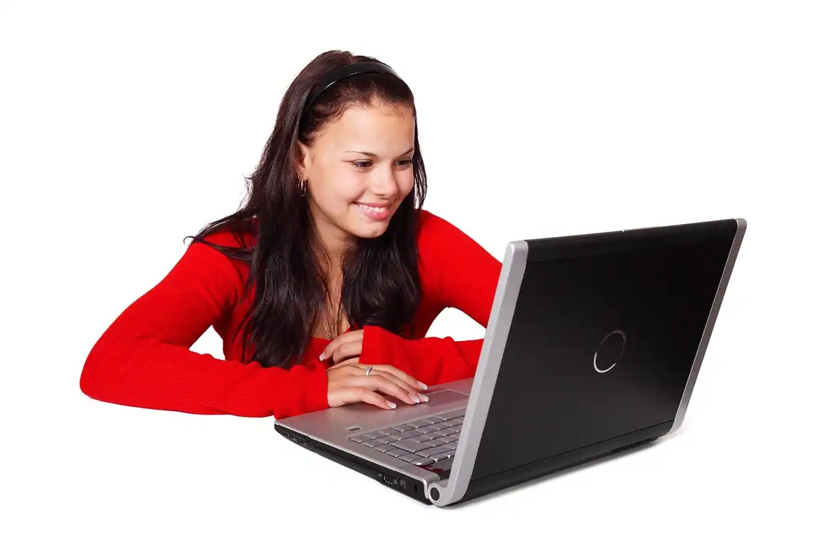 O tânără zâmbitoare privește ecranul unui laptop, sprijinită pe coate