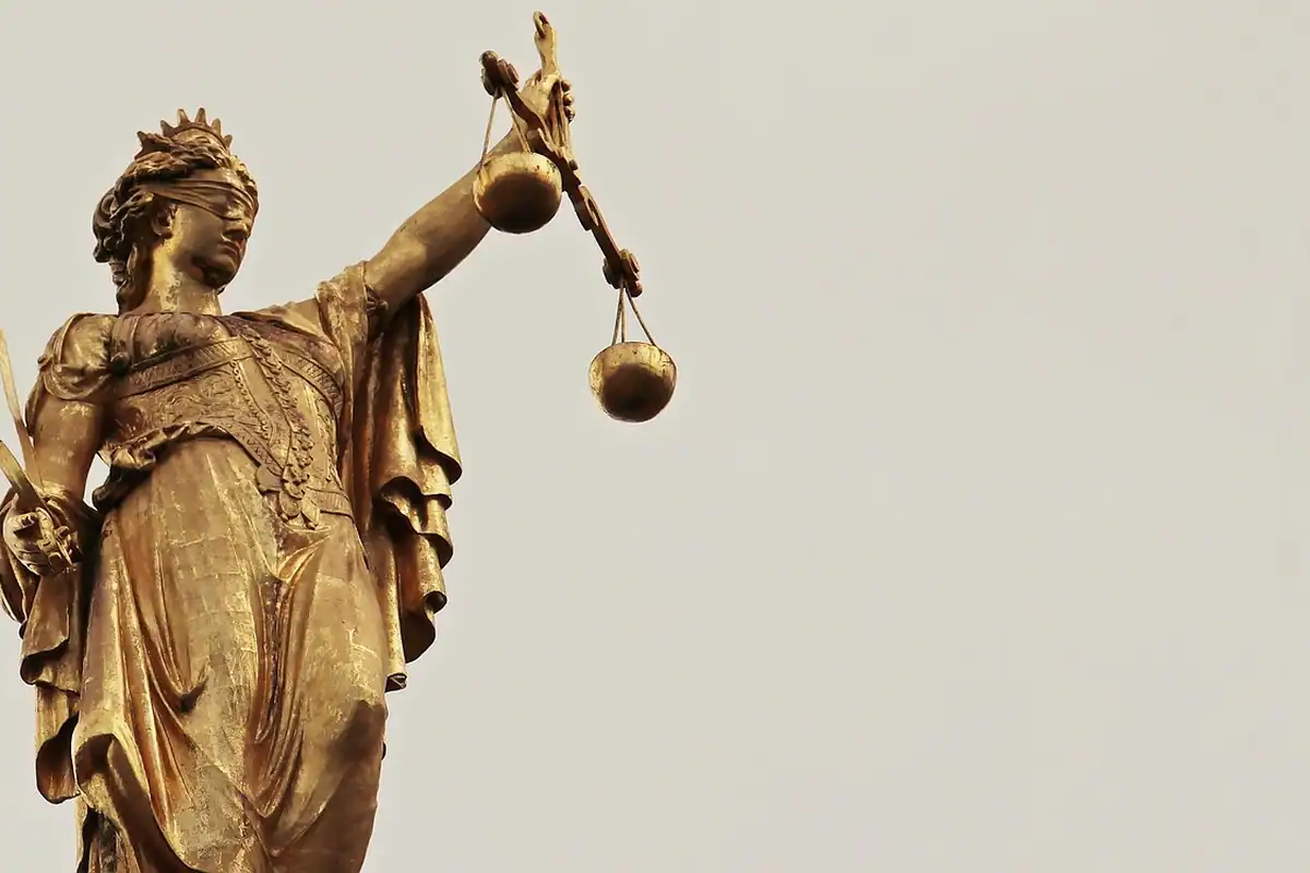 Statuie aurie a Justiției, cu balanța în mână, pe fundal neutru