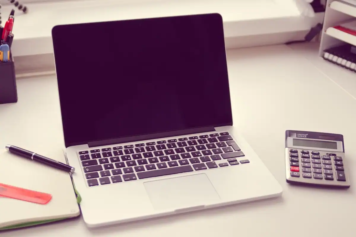 Laptop deschis, calculator și agendă, așezate pe un birou luminos