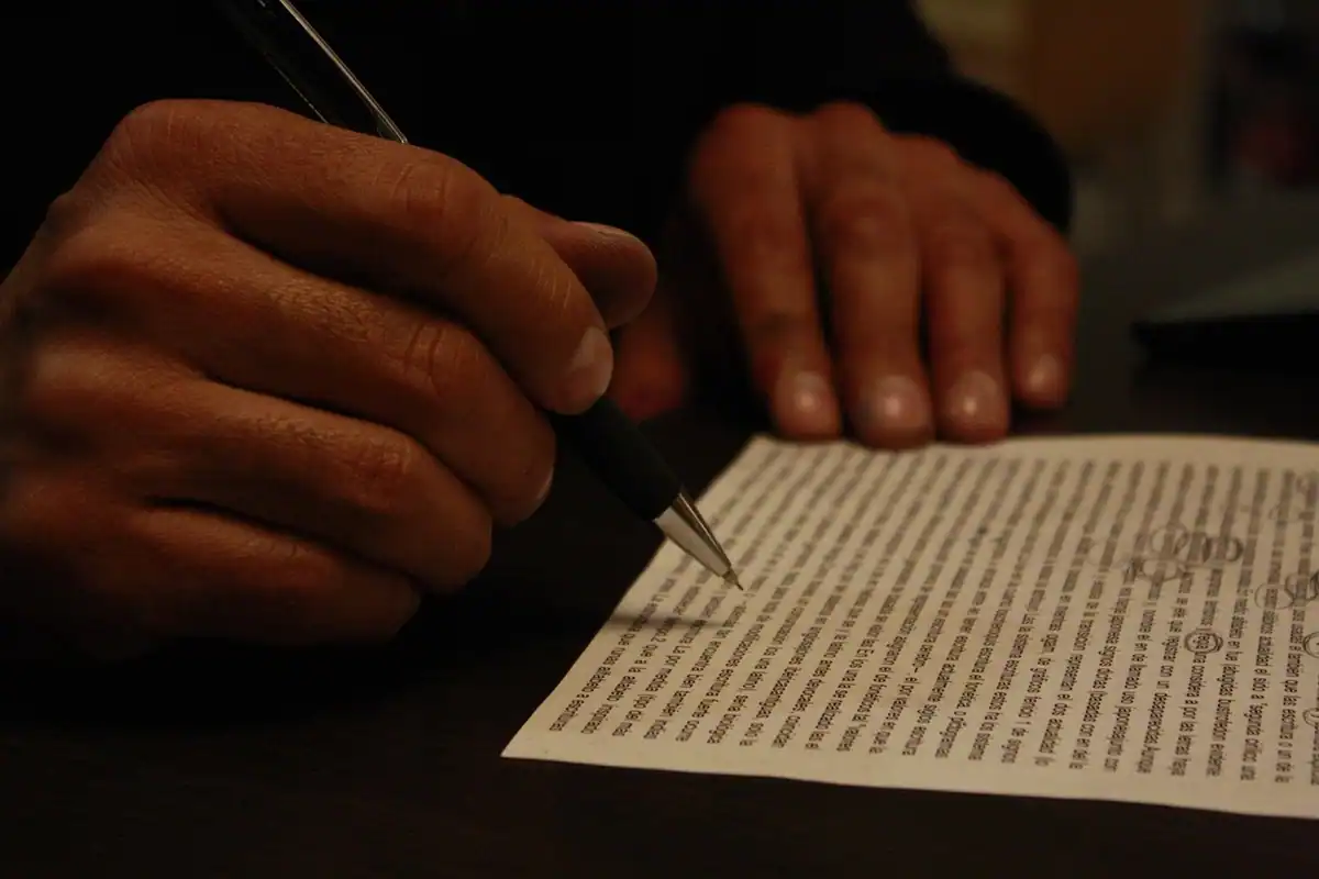 Mâini în lumină caldă scriu cu pixul pe o foaie plină de text