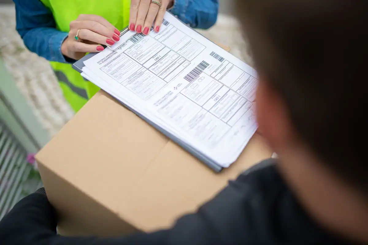 O persoană ține un formular de livrare deasupra unui colet de carton
